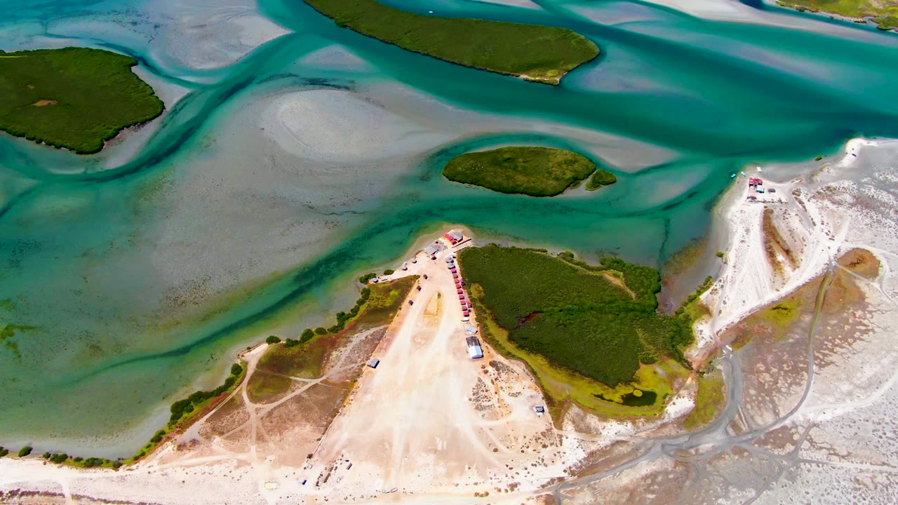 Top-down La Bocana view with broad shallow sand flats, darker turquoise water paths, a green island near the center, and no visible people.