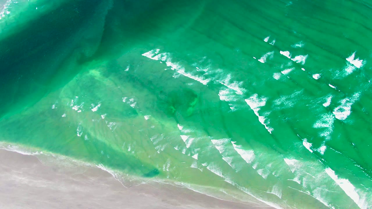 White foam streaks across shallow green water near sand