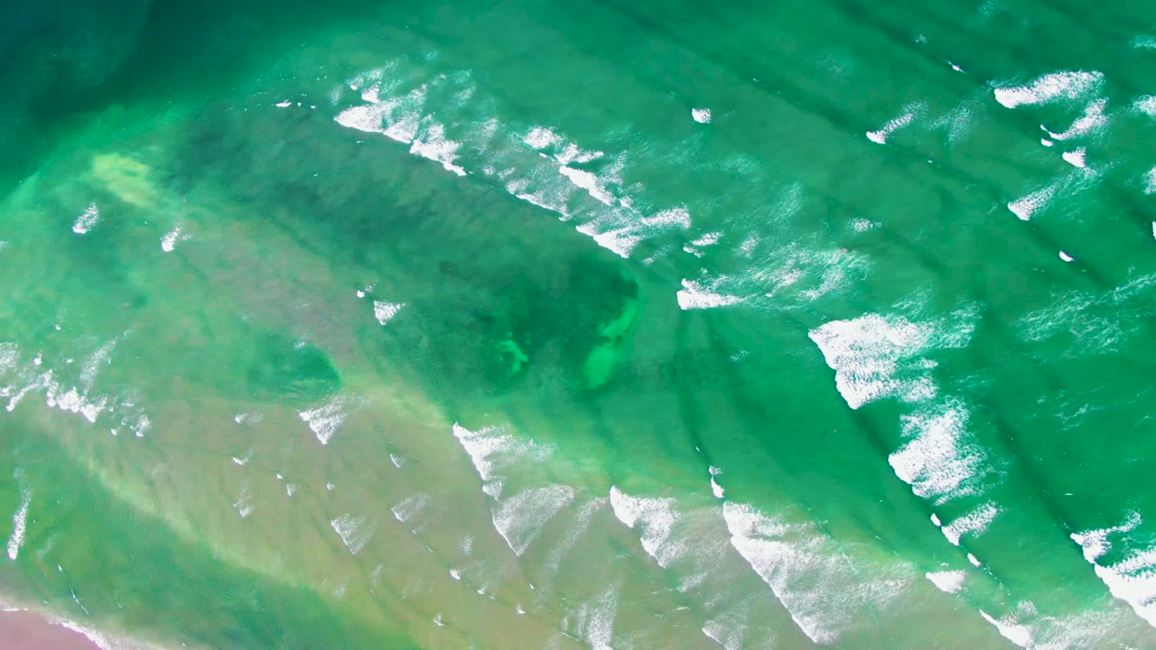 Blue-green shallow water with foam streaks and seabed visible below.