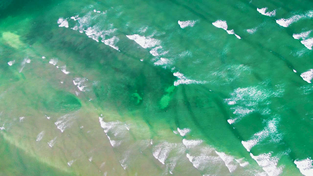 Green sea surface with pale shallows and broken foam lines.