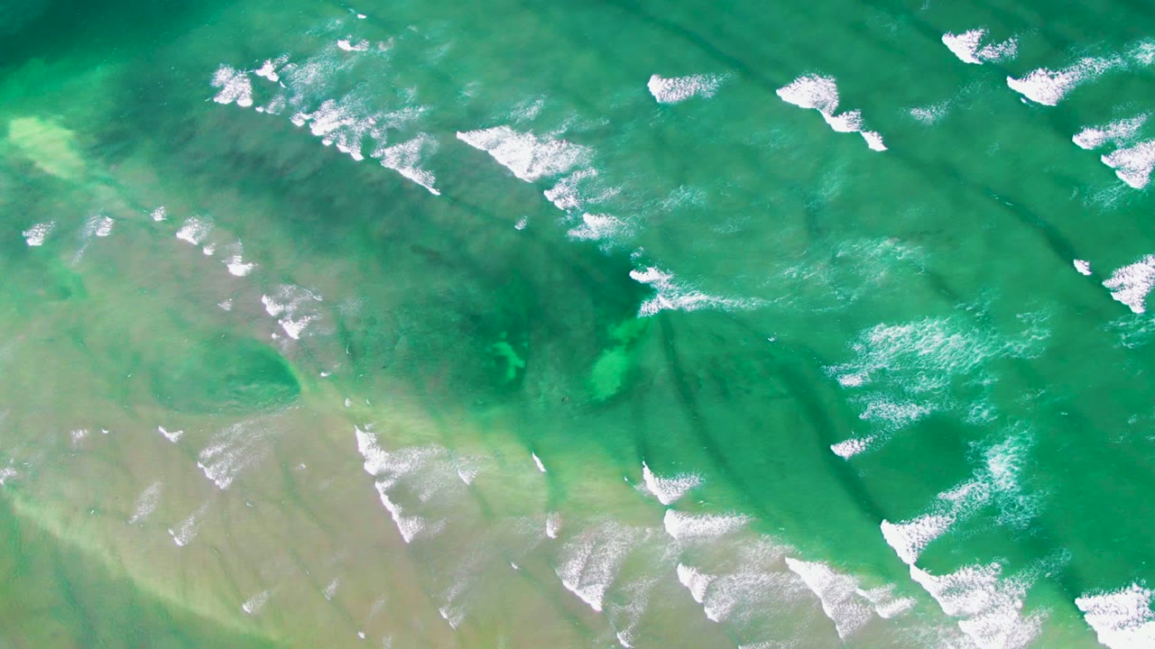 Aerial shot of turquoise water off La Bocana with white foam crests spread across the upper and lower portions of the frame and no visible people.