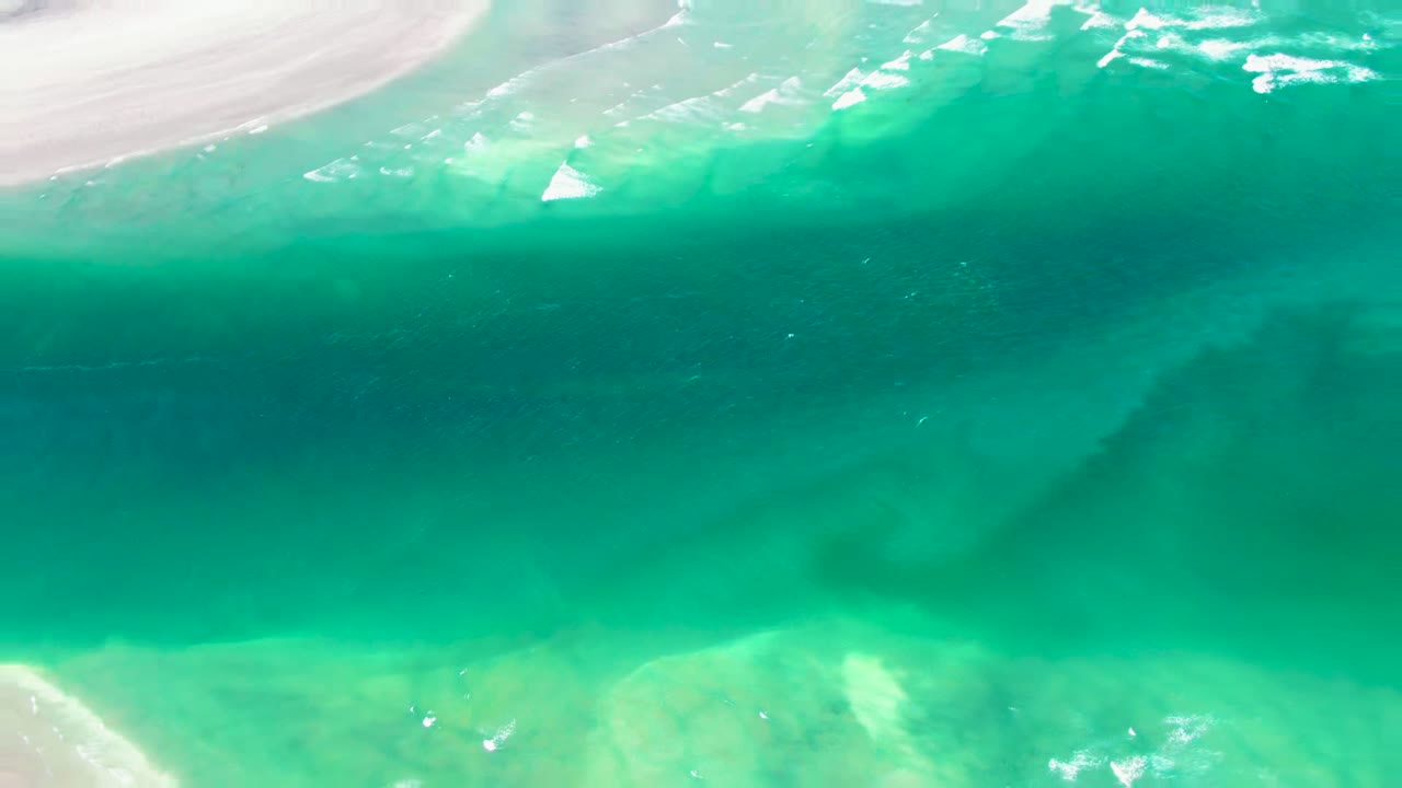 Overhead view of turquoise water washing over pale sand at La Bocana, Baja California Sur, with white foam near the upper shore and no visible people.
