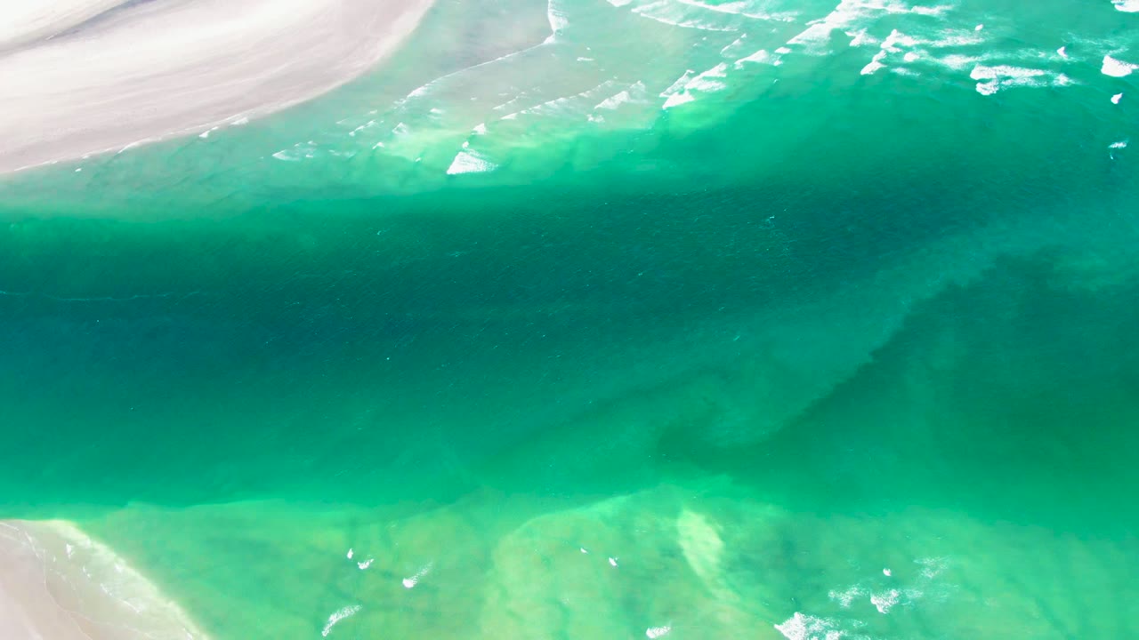 Clear green-blue water with sandbars and white foam streaks.