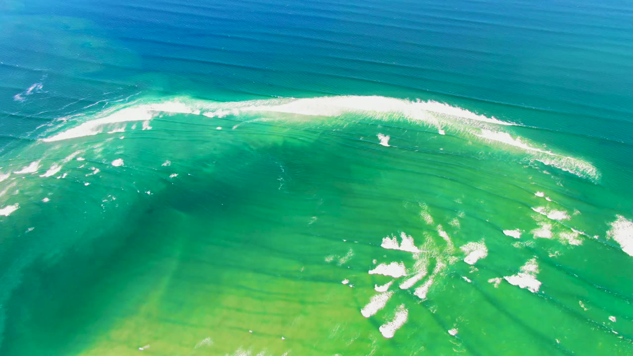 At 0:00 in La Bocana, Baja California Sur, a curved white ocean wave breaks across blue and green water with dark seabed bands below and no visible people.