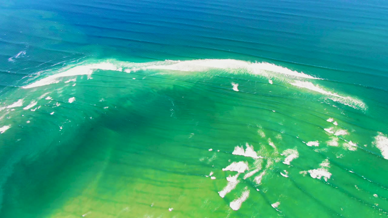 At 0:02 in La Bocana, Baja California Sur, a bright white crest runs diagonally across transparent green-blue water with scattered foam below and no visible people.
