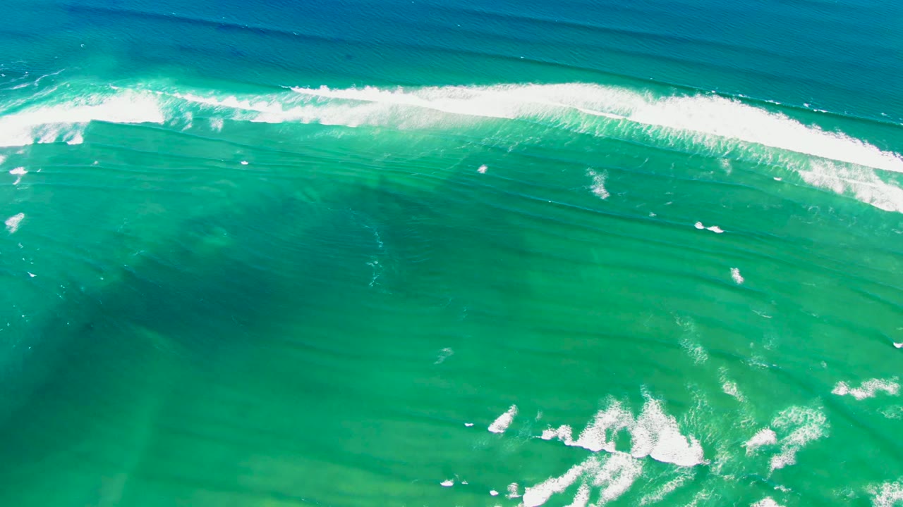Overhead view of turquoise ocean at La Bocana, Baja California Sur, with a white foam wave band near the top and darker water patches below, no visible people.