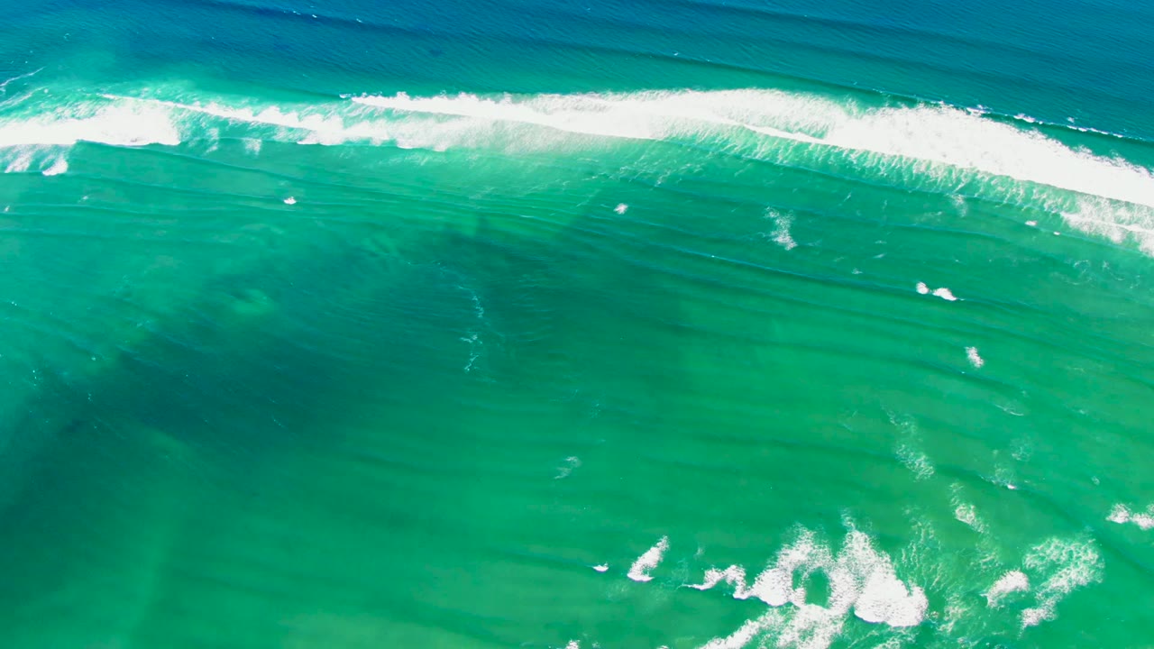 White wave foam stretches across the upper frame over clear green-blue water.
