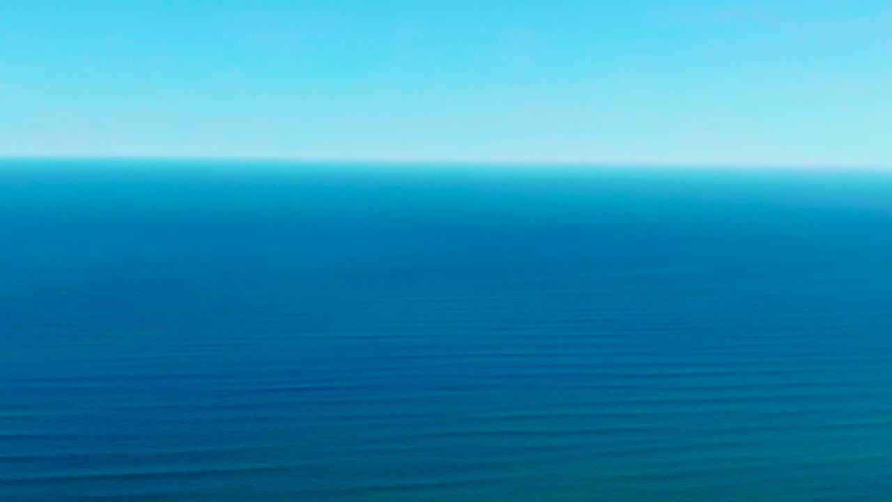 Opening frame of the ocean off La Bocana, Baja California Sur, with blue water, faint parallel wave lines, a level horizon, pale sky, and no visible people.
