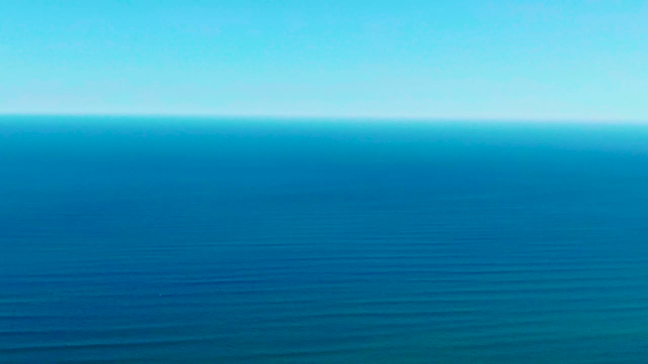 Calm ocean with subtle wave bands below a pale blue sky