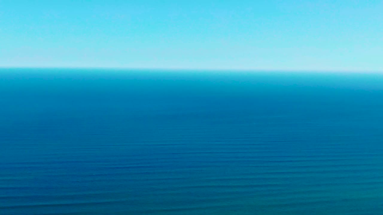 A broad view of open sea near La Bocana shows darker blue water in the foreground, lighter blue toward the horizon, clear sky, and no visible people.