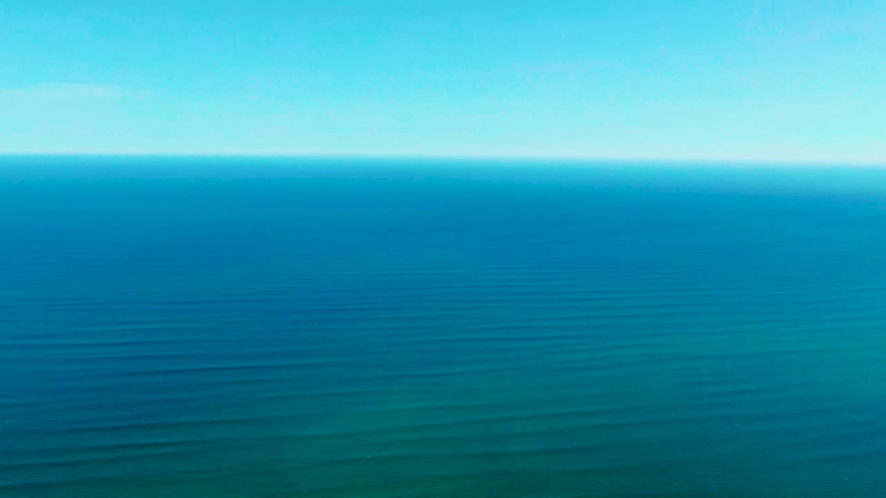 Wide aerial view over the ocean at La Bocana, Baja California Sur, with a clear blue horizon, faint parallel swell lines, and no visible people.
