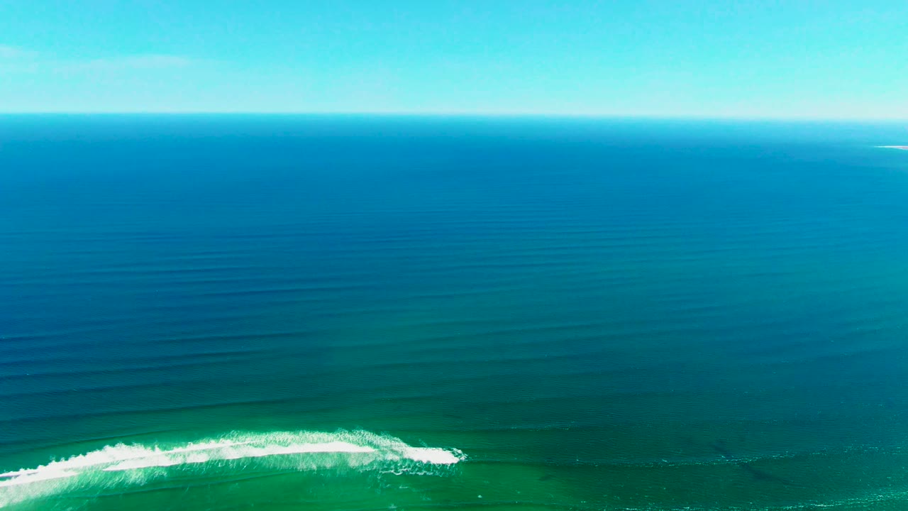 White surf line spreads across green-blue water under a distant horizon.