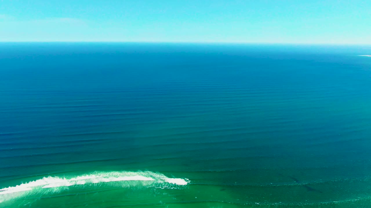 The La Bocana wave curls in a bright white band over turquoise shallows, with darker blue water leading to a straight horizon and no visible people.