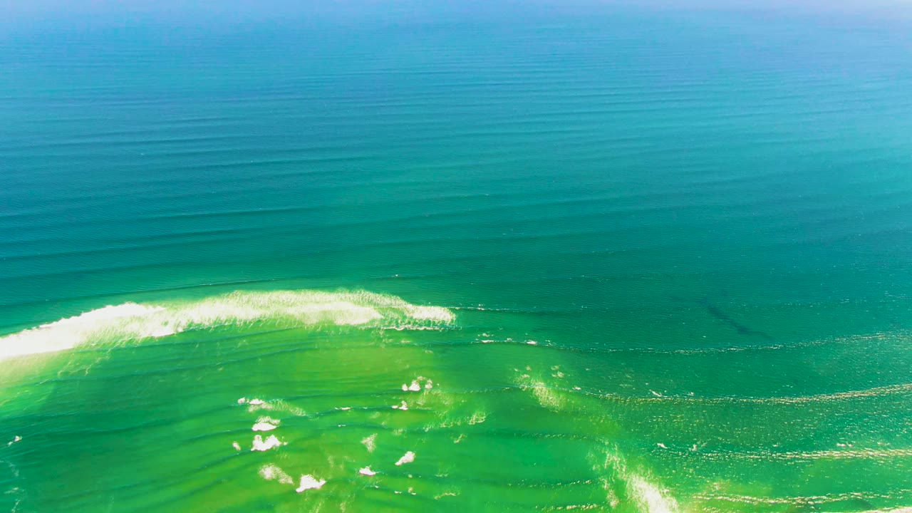 White surf line curls across clear green water beneath deeper blue ocean.