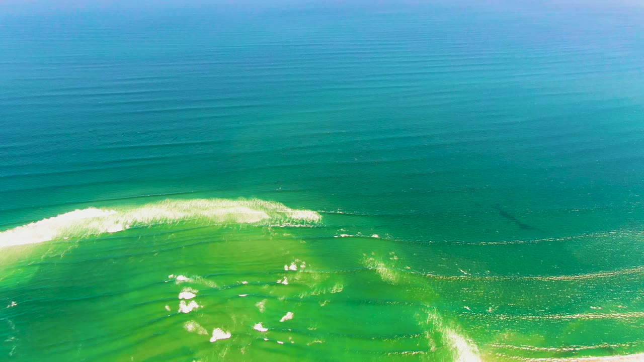 A foamy white crest runs diagonally through clear turquoise water at La Bocana, with darker blue water filling the upper frame and no visible people.