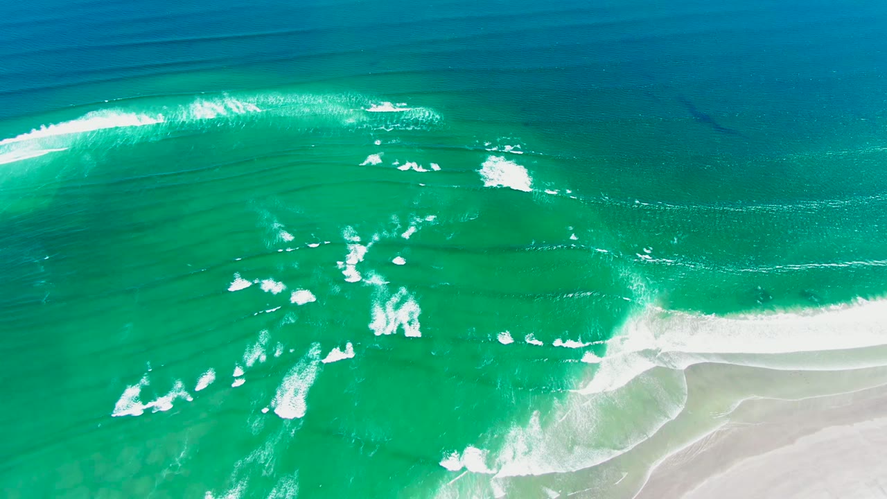 Overhead drone view of turquoise surf with a stronger white break near the lower right sandy shore at La Bocana, Baja California Sur, and no visible people.