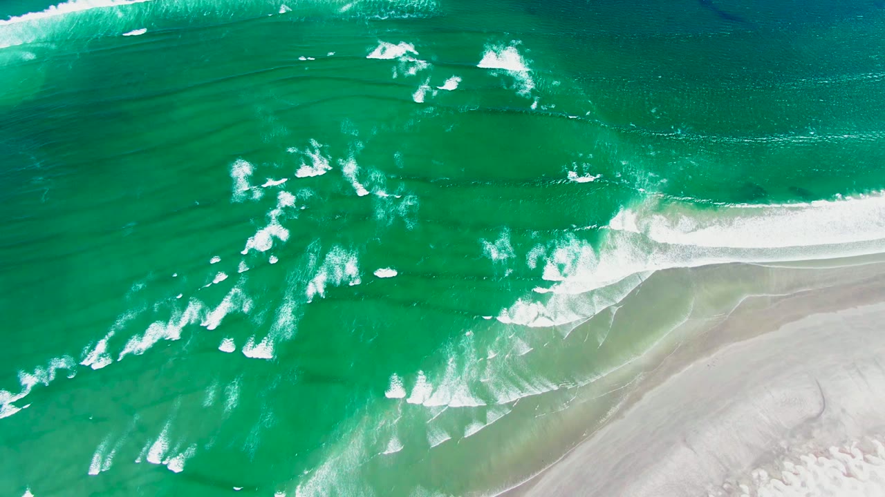 White foam bands move across turquoise ocean toward sand