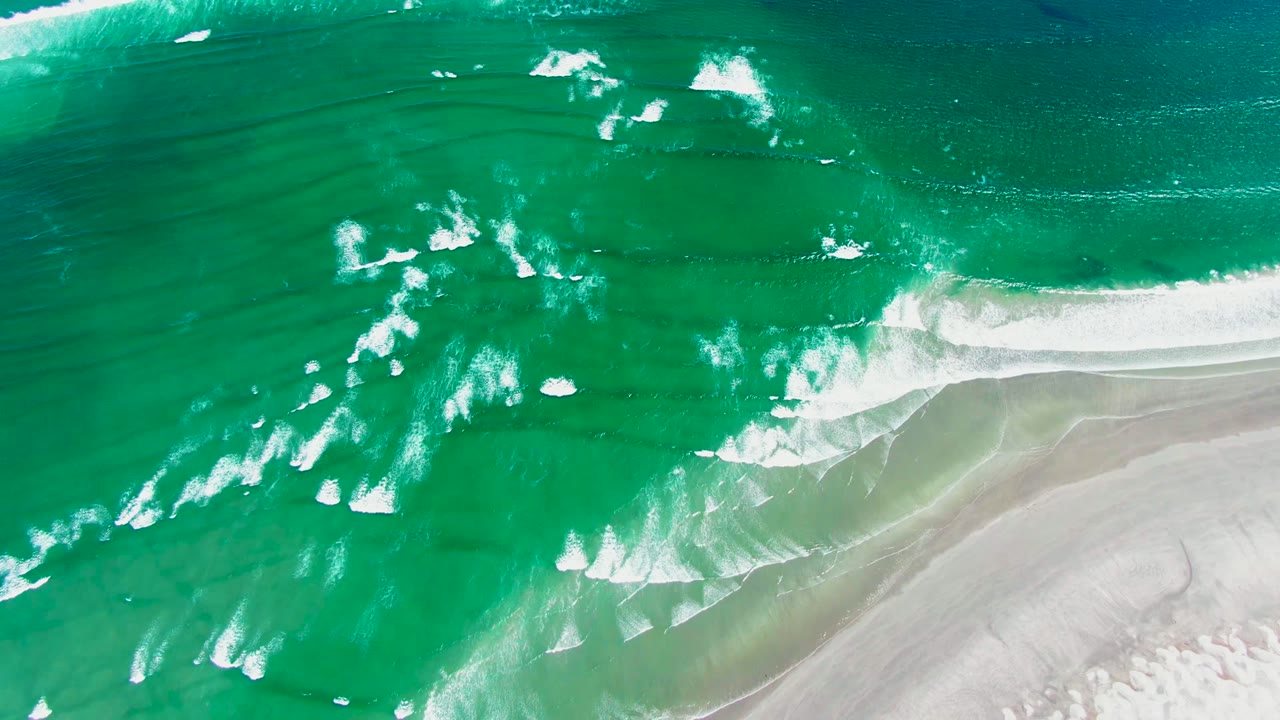 Top-down drone frame at La Bocana showing a brighter breaking wave curling along the edge of the light sandy beach, with no visible people.