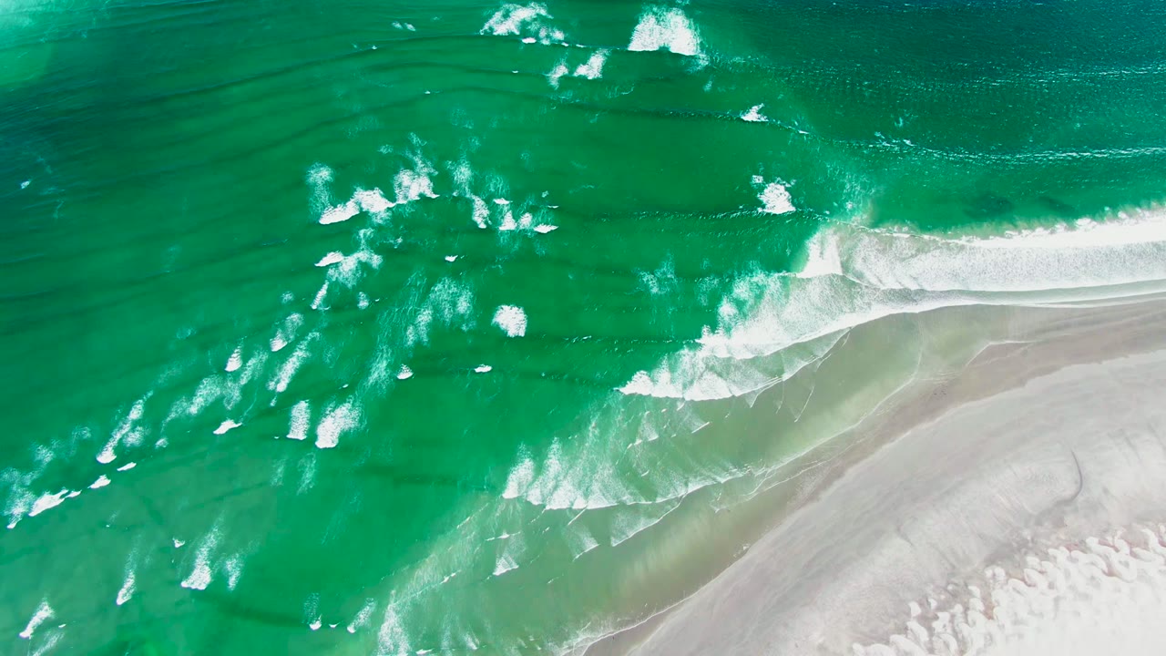 Overhead view of turquoise surf and white foam approaching pale sand at La Bocana, Baja California Sur, with no visible people.