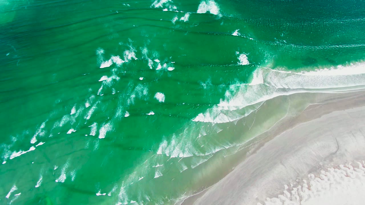 White foam lines spread across turquoise water beside sand.