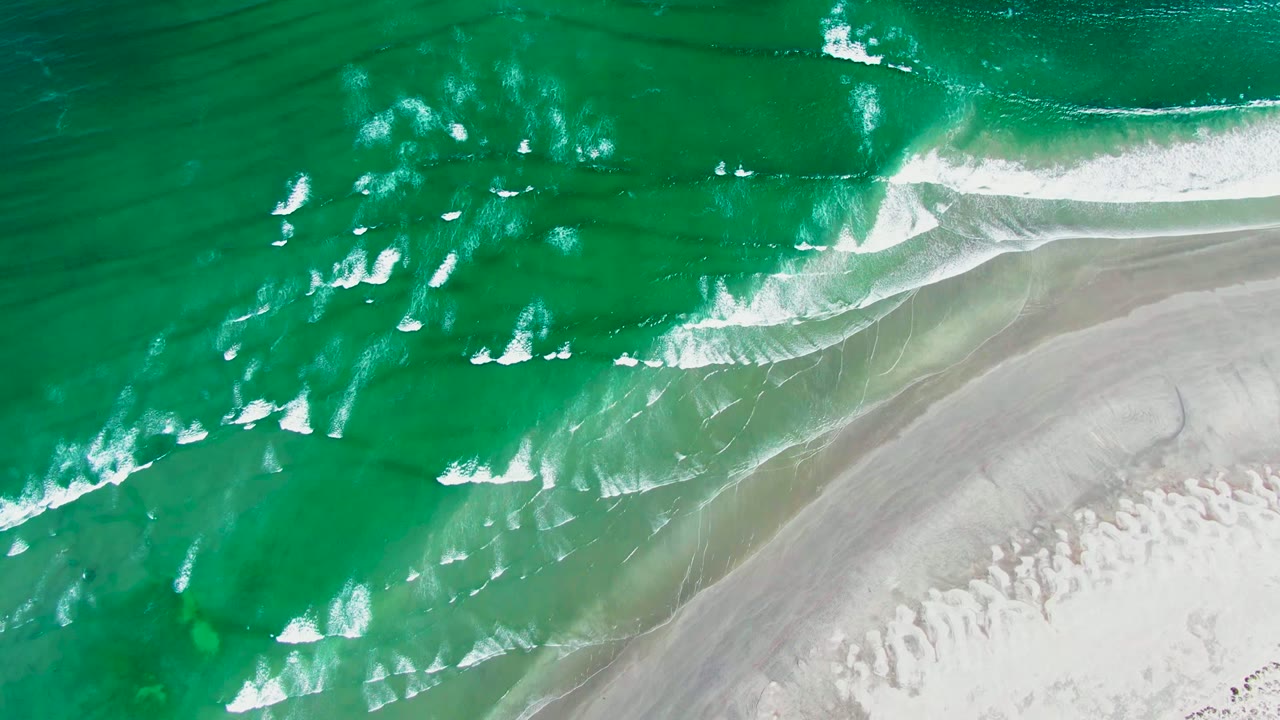 Aerial shoreline frame from La Bocana, Baja California Sur showing diagonal surf bands, darker green water above them, pale sand below, and no visible people.