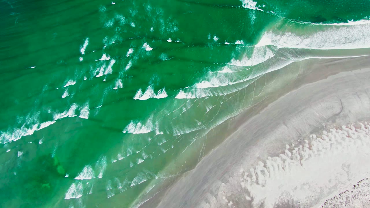 Overhead view of green ocean waves breaking diagonally onto pale sand at La Bocana, Baja California Sur, with no visible people.