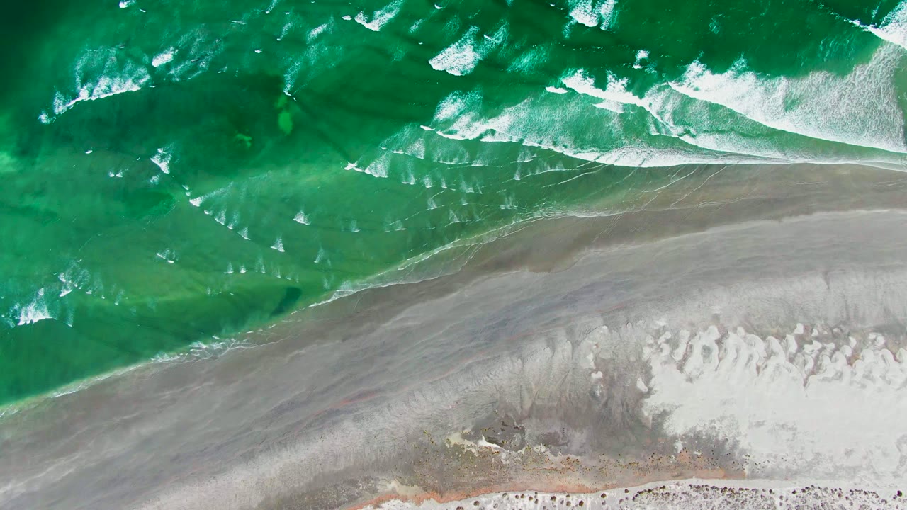 Foamy wave band spreading across a sandy shoreline.