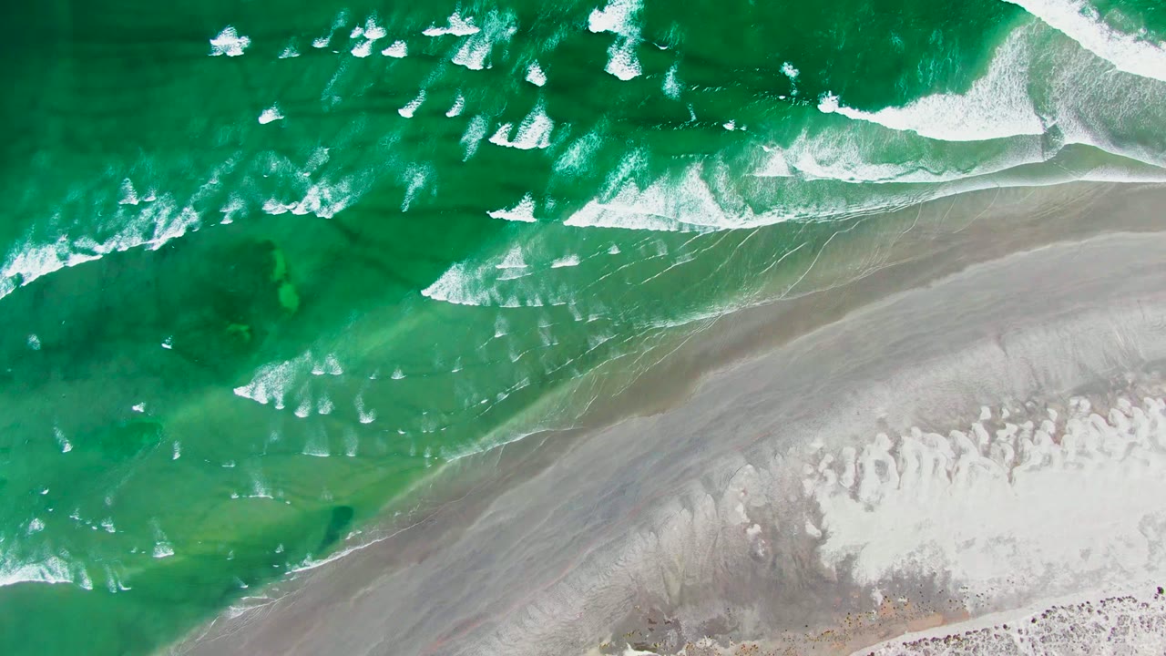 Overhead frame of green La Bocana surf breaking into white foam beside wet gray sand and pale beach, with no visible people.