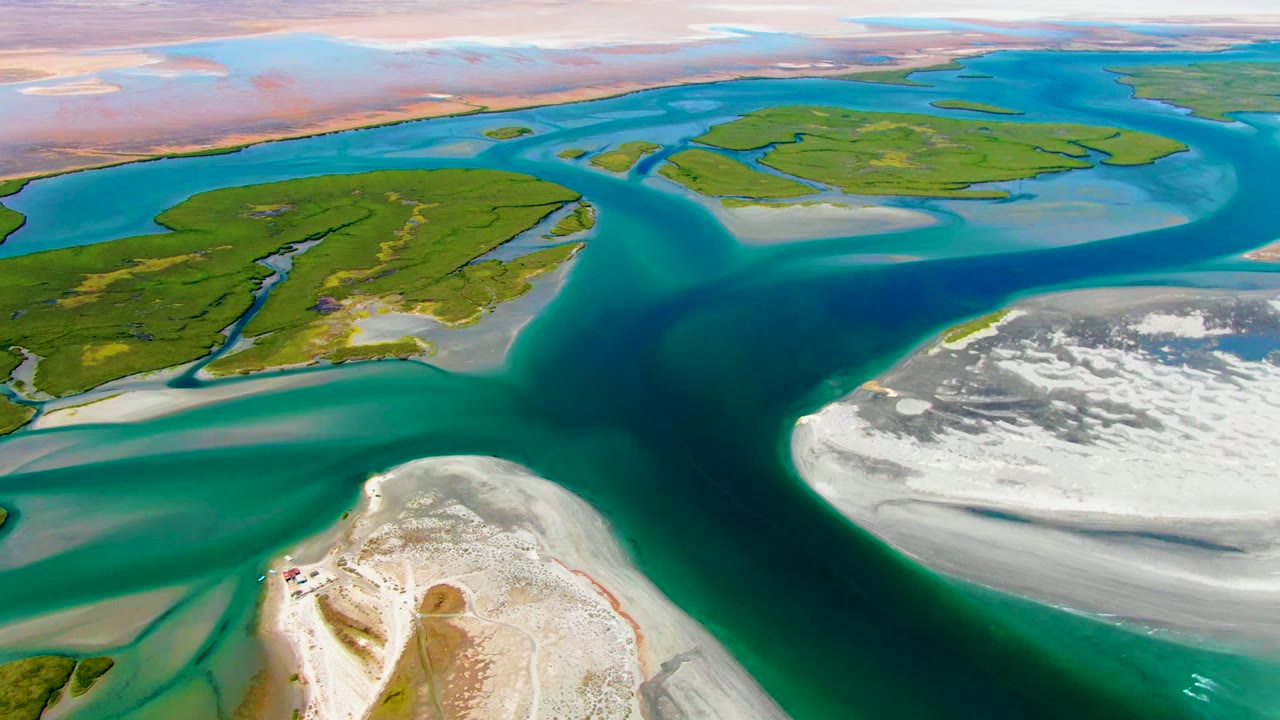 Aerial coastal channels with green islands and white sandbars under soft light.
