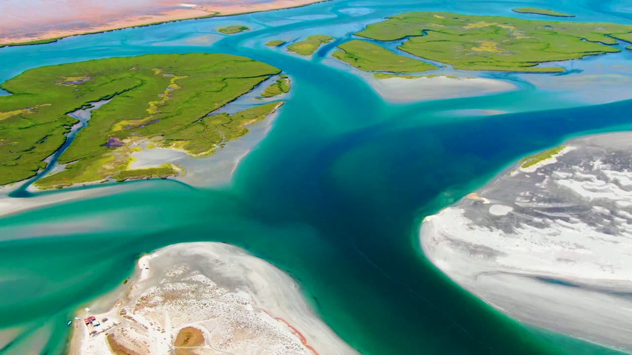 Opening aerial frame over La Bocana, Baja California Sur, showing deep blue water between green islands and white sandbars with no visible people.