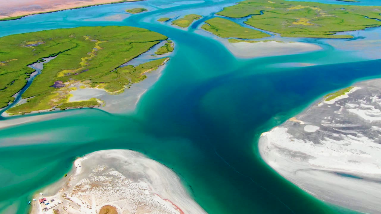 Deep blue water channel between green islands and white sand flats.
