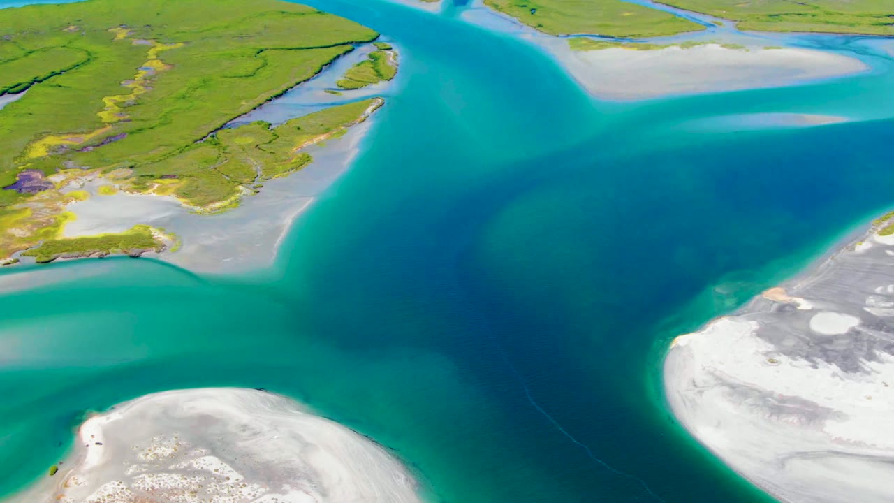 Aerial coastal channel with blue water between sandbanks and green land.