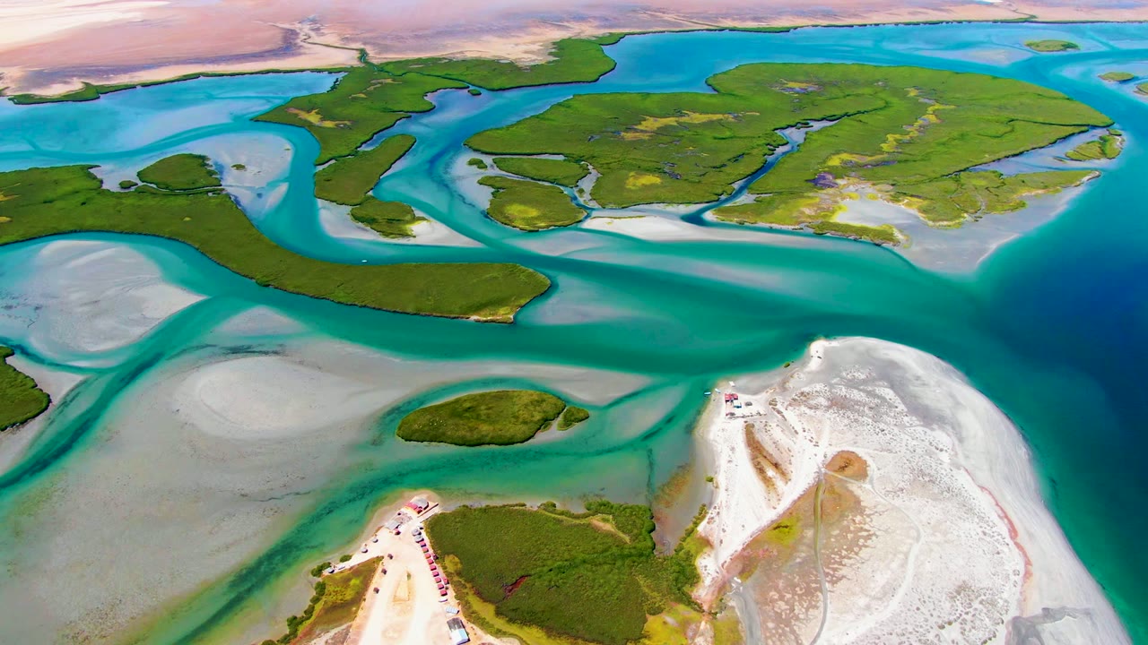Drone view of green coastal islands divided by blue water channels and pale sandbars.