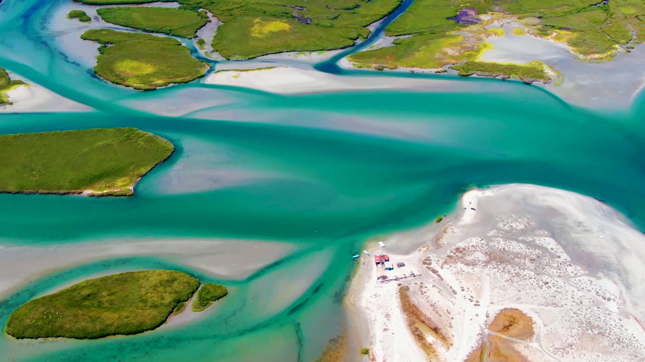 Opening aerial frame over La Bocana, Baja California Sur, with turquoise water dividing green islands and a white sandy shore at right, no visible people.