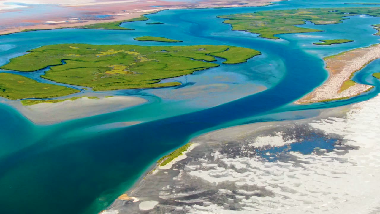 Blue and turquoise water surrounds low green islands beside a white shoreline.