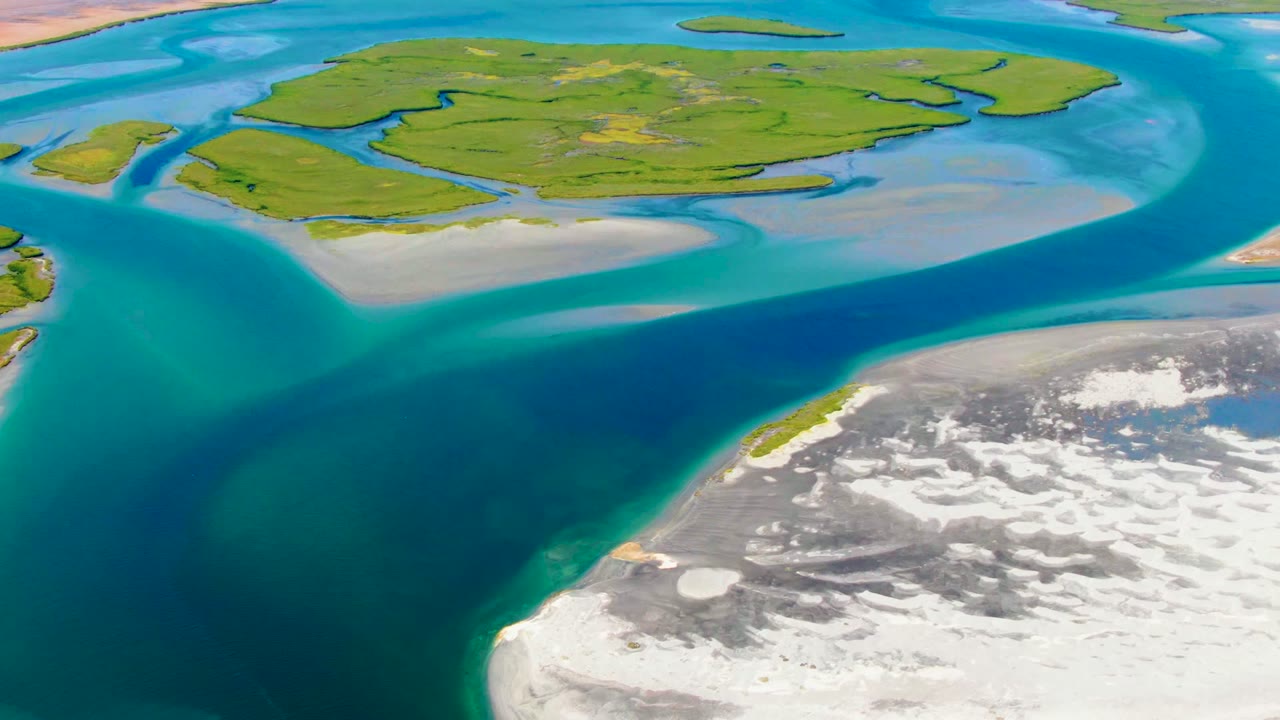Aerial view over La Bocana, Baja California Sur, with a deep blue channel between green islands and pale sandbars, no visible people.