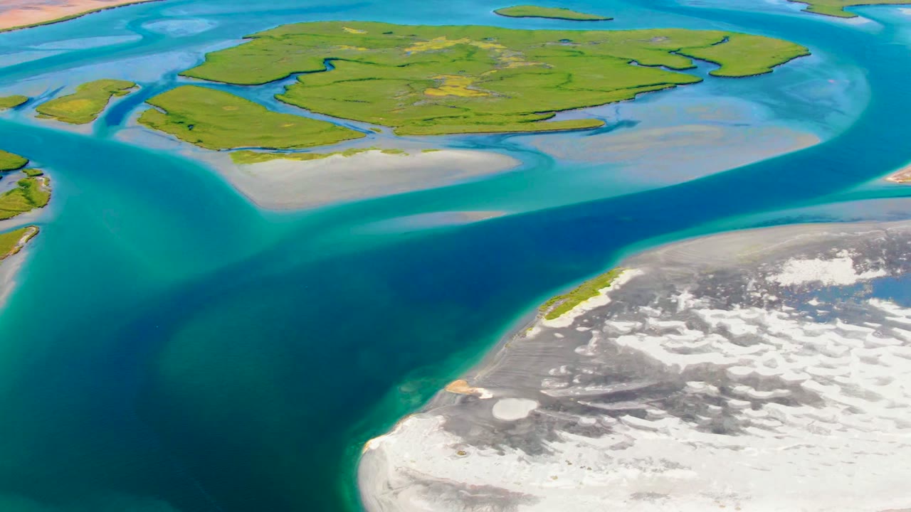 Drone view of a blue channel cutting between low green islands and sandy flats.