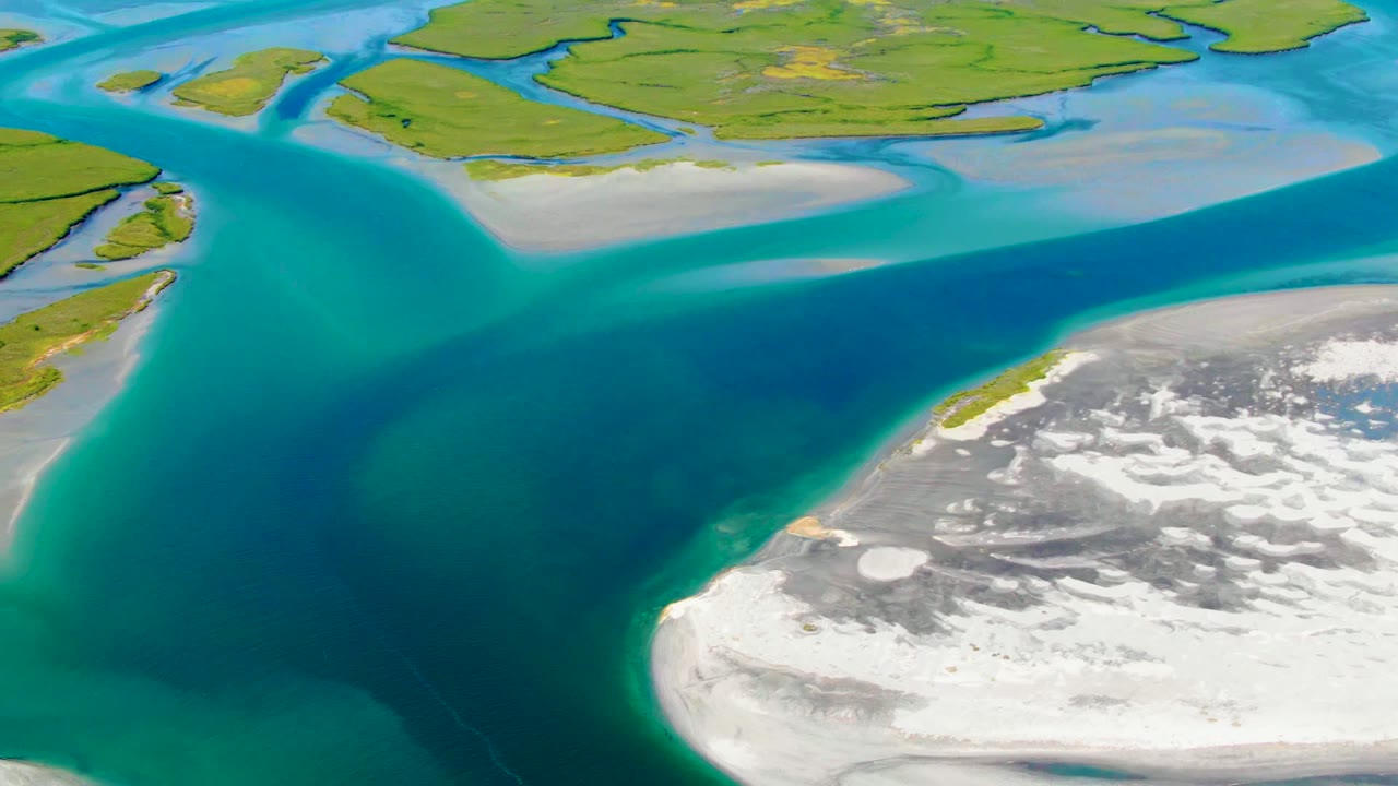 Overhead aerial frame from La Bocana, Baja California Sur, showing turquoise coastal water between green land at the top and a pale white-gray shore edge at lower right, with no visible people.