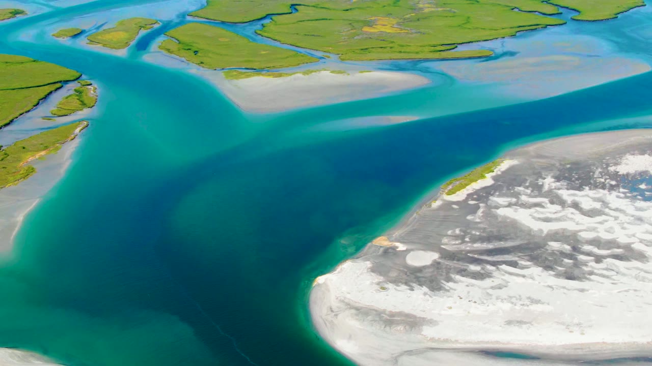 Aerial coastal channel with green land above and pale shore below.