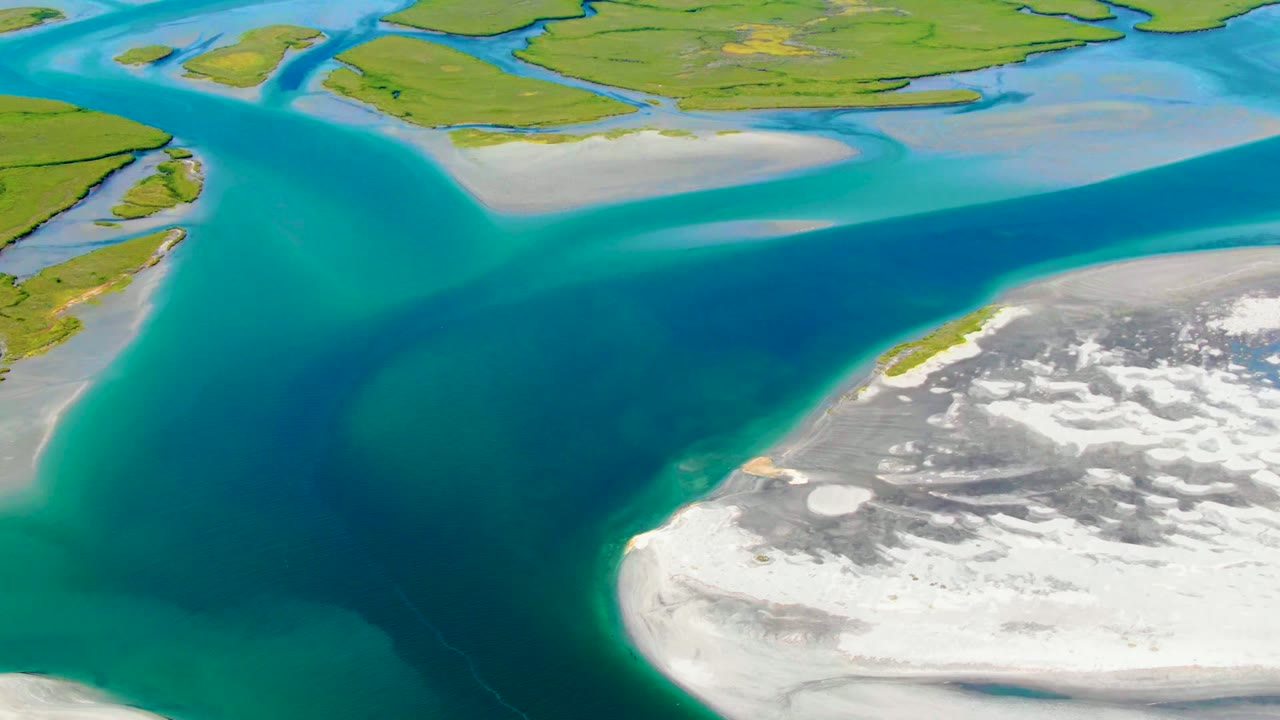 At two seconds, the La Bocana frame shows turquoise water curving around a white-gray shore edge, with green land and narrow water cuts across the upper background and no visible people.