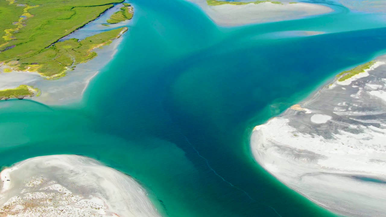 La Bocana aerial frame with curved turquoise water wrapping around bright white sand, darker water through the middle, and green land at the top, with no visible people.