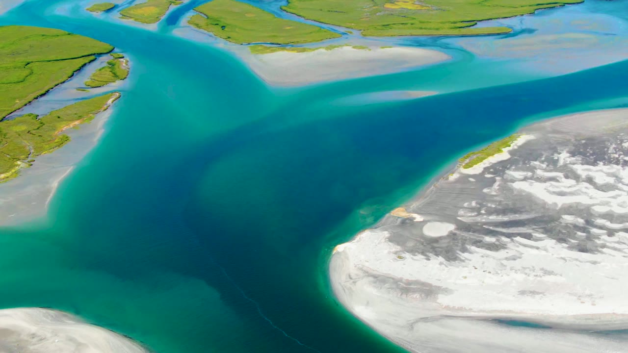 Opening aerial frame over La Bocana, Baja California Sur, with turquoise water crossing between green land and white ice or snow patches, no visible people.