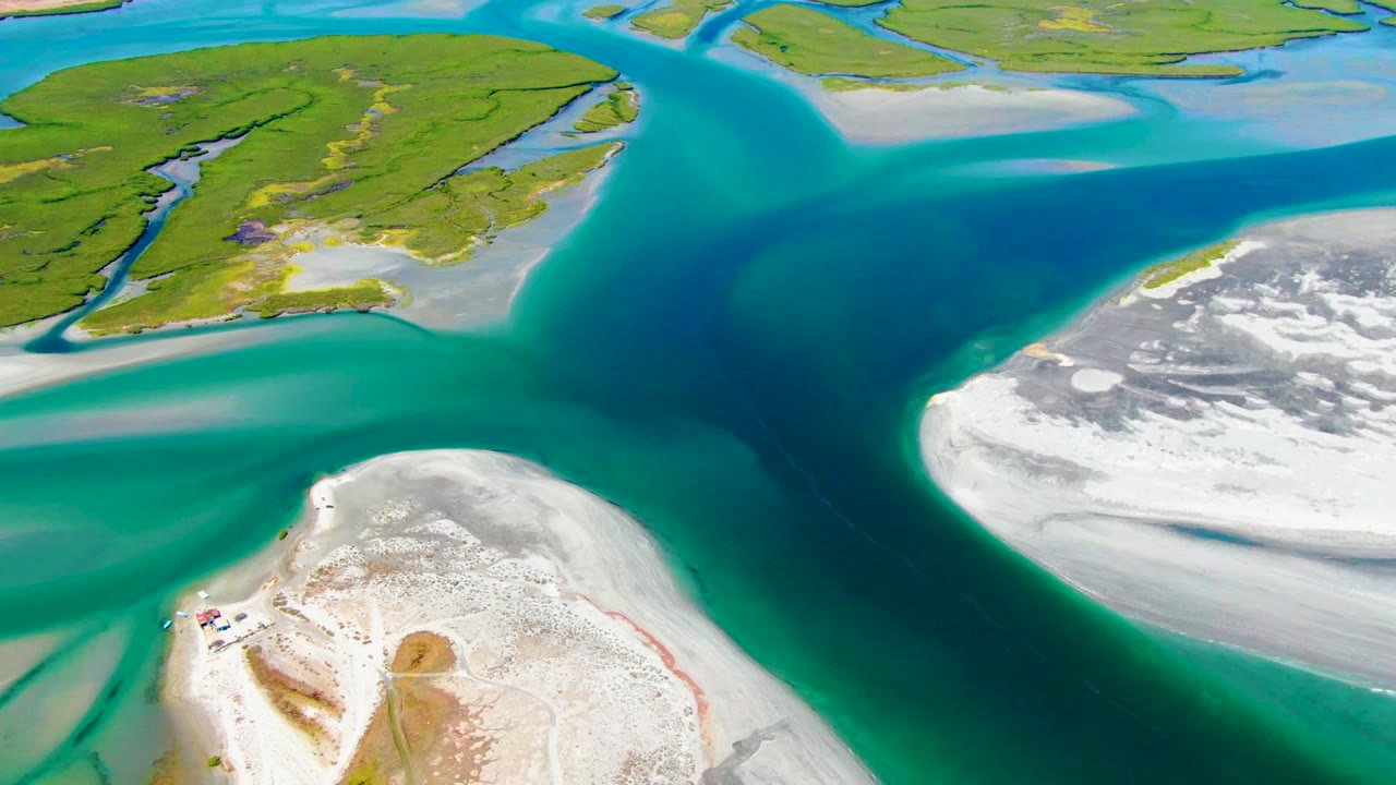 High aerial frame from La Bocana showing white sand flats in the foreground, turquoise water through the center, green wetland islands at the top, and no visible people.