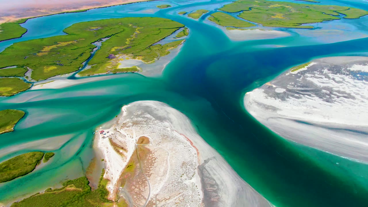 Aerial frame from La Bocana, Baja California Sur, showing turquoise tidal channels splitting around white sand shoals with green islands beyond and no visible people.