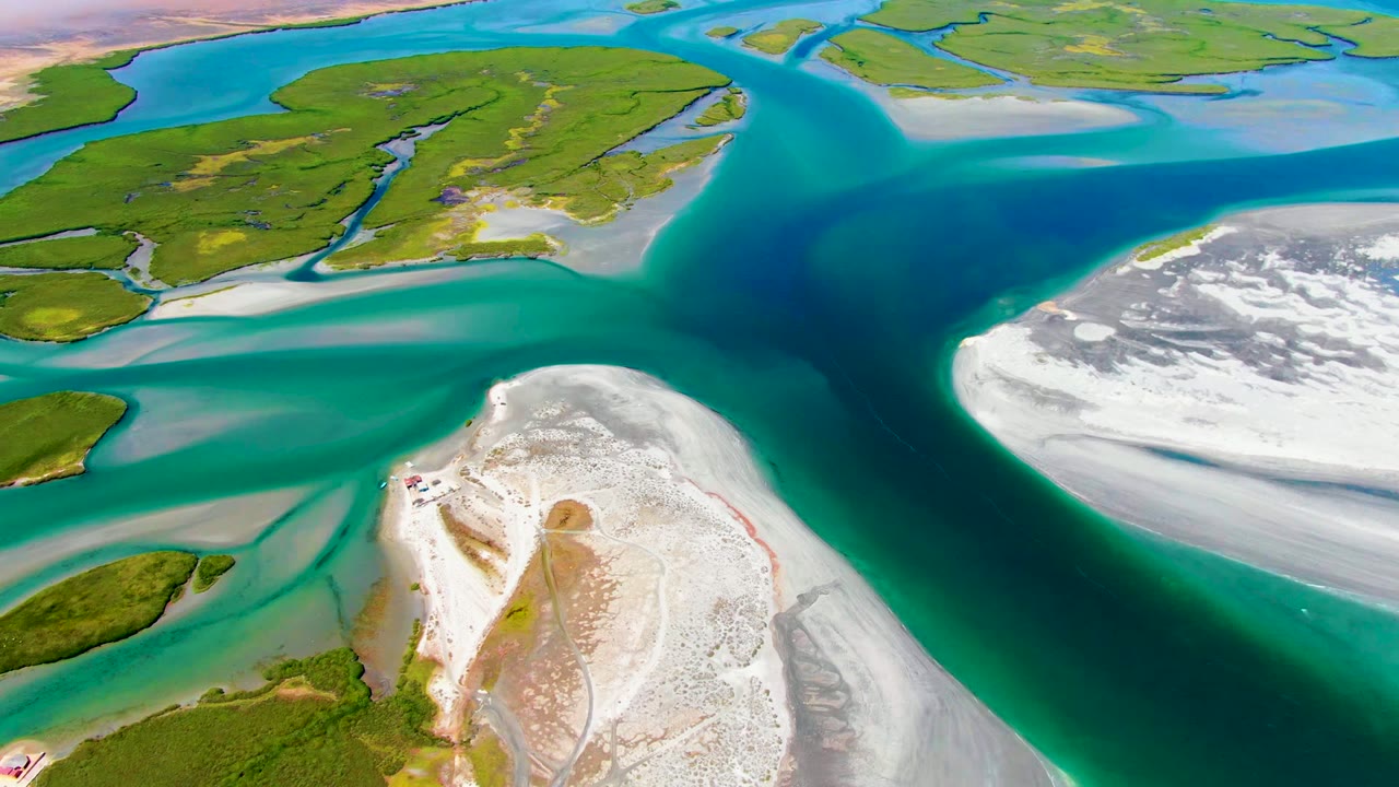 Aerial frame from La Bocana, Baja California Sur, showing green islands across the upper frame, broad white shoals at right, turquoise water paths, and no visible people.