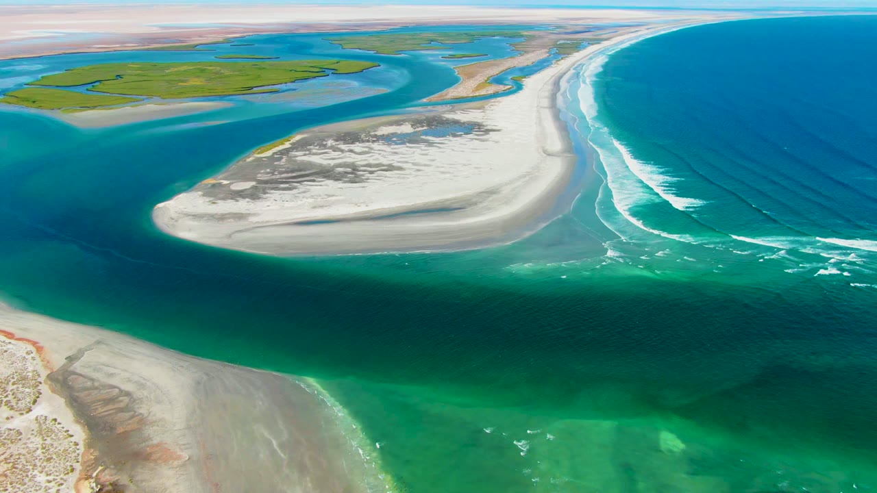Sandbar and surf lines seen from above over clear coastal water.