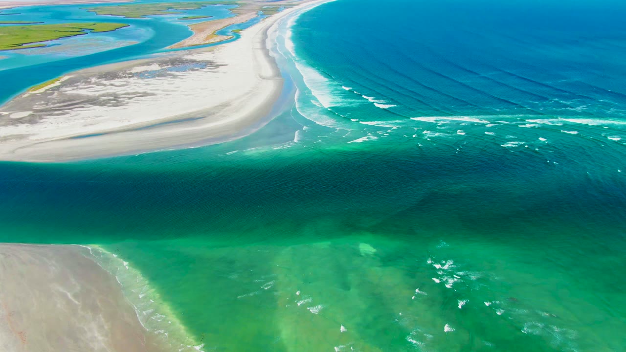 Aerial frame from La Bocana, Baja California Sur, Mexico, showing deep blue water, turquoise shallows, pale sandbars, and white wave lines with no visible people.