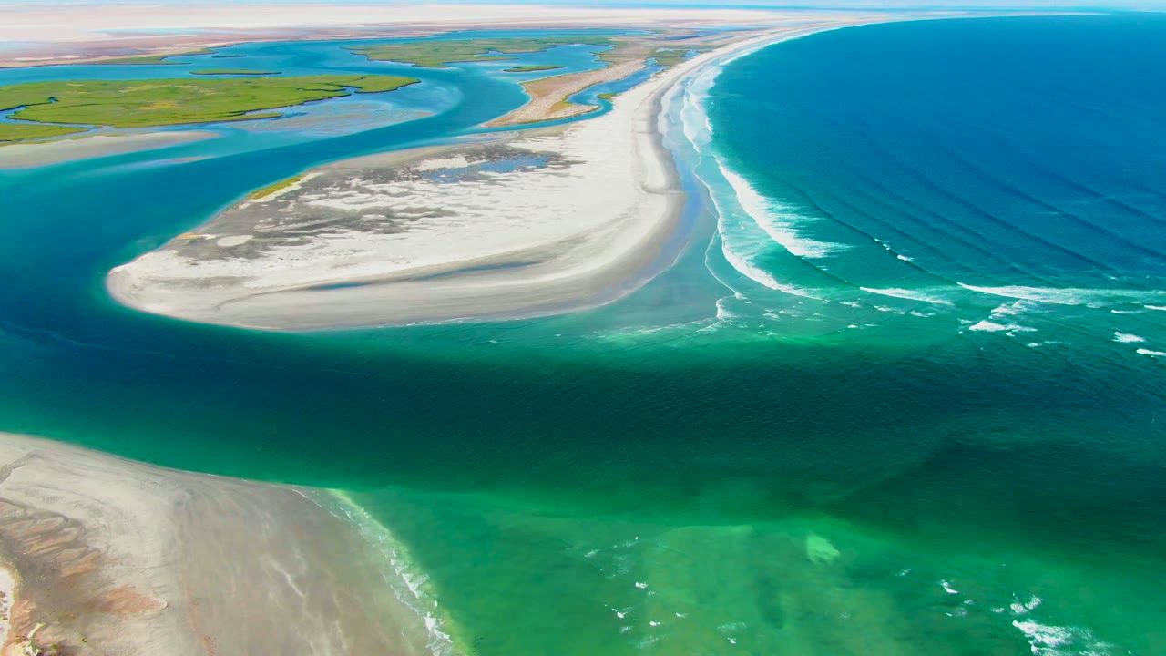 Aerial frame from La Bocana, Baja California Sur showing a pale sandbar between turquoise shallow water and deep blue ocean, with no visible people.