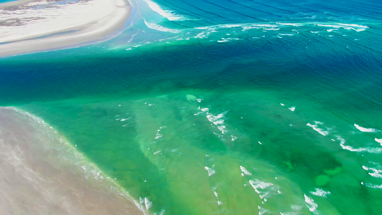Clear green-blue shallow water with foam lines moving over sand.