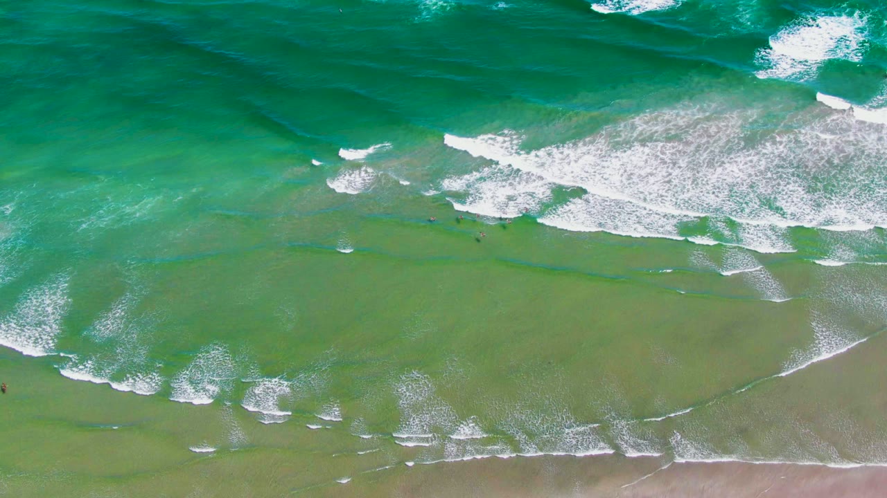 Breaking white surf rolls across green water toward the beach.